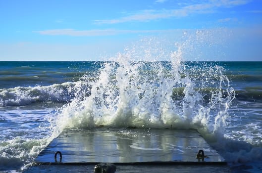 Powerful waves of the sea foam, breaking the concrete pier