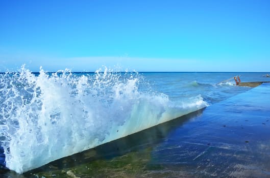 Powerful waves of the sea foam, breaking the concrete pier