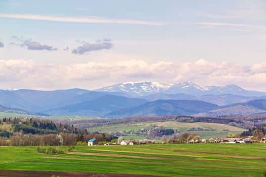 Spring fields and orchard blossom on foothills. Sunny green spring landscape. Spring fields and blooming trees. Village and town behind foothills