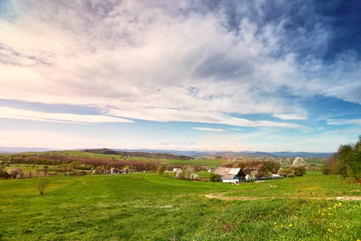 Sunny spring day in village and town on foothills. Mountains on background. Sunny green spring landscape.