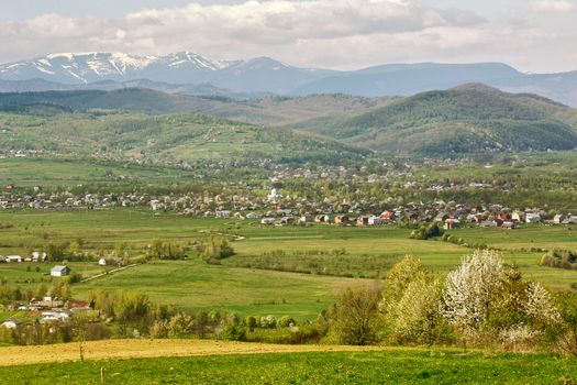 Sunny spring day in village and town on foothills. Mountains on background. Sunny green spring landscape.