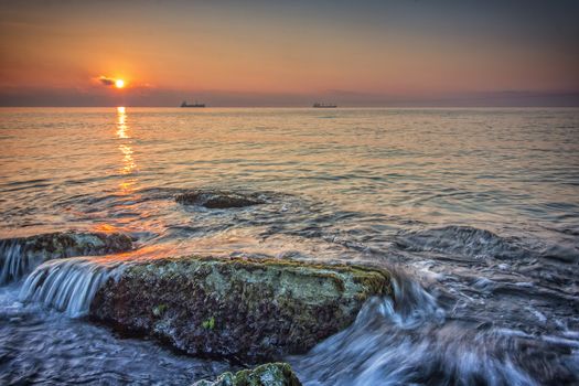 Sea sunrise. Beauty sea rocks with slow shutter and waves flowing out.