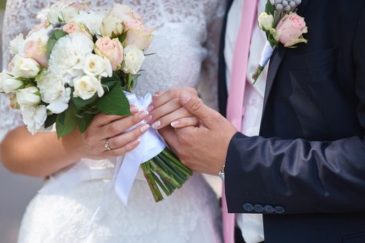 groom holds his brides hand and a wedding bouquet close up