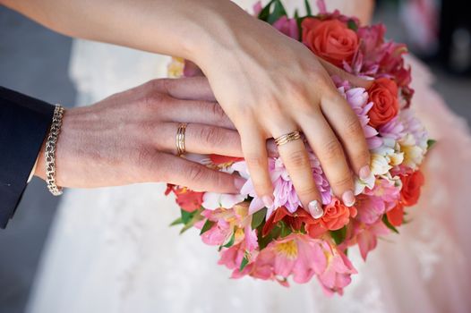 bride and groom hand with rings on wedding bouquet.