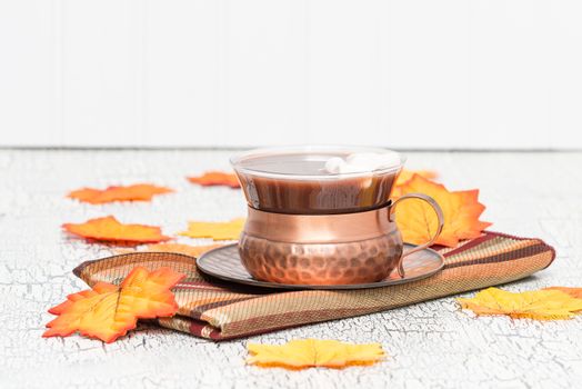 Cup of creamy hot chocolate with colorful autumn leaves.