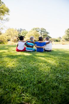 Kids are sitting on the grass together during a sunny day at park 