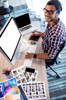 Attractive hipster smiling at camera while working at desk in studio