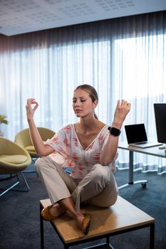 Businesswoman doing yoga with hands in the air at office