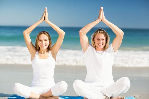 Portrait of happy man and woman performing yoga on beach