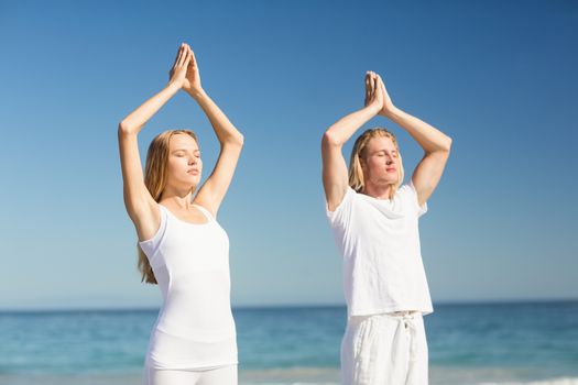 Man and woman performing yoga on beach