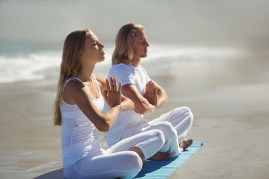 Man and woman performing yoga on beach