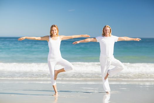 Portrait of happy man and woman performing yoga on beach