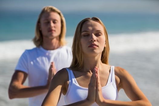 Man and woman performing yoga on beach