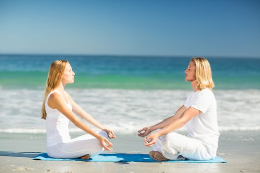 Man and woman performing yoga on beach