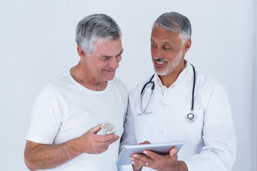Male doctor showing medical reports to senior man on digital tablet in hospital