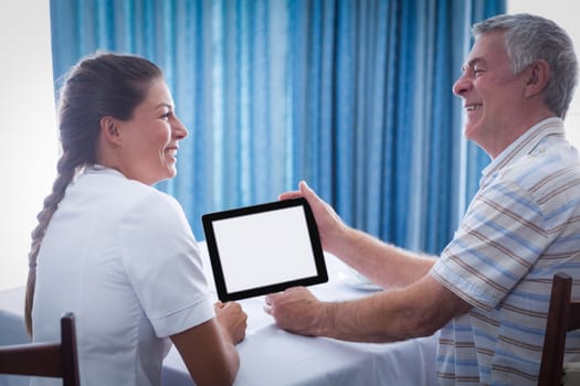 Senior man and female doctor using digital tablet at home