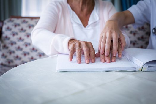 Mid section of female doctor helping a blind patient in reading the braille book