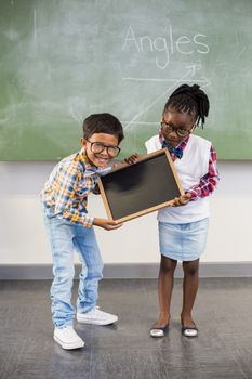 Portrait of two smiling school kids holding slate in classroom at school