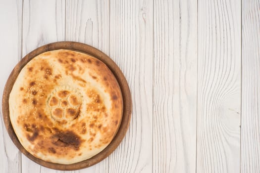 Uzbek flat cake on the board and an old white wooden table. Top view.