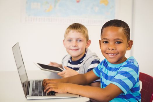 Portrait of smiling kids using a laptop and digital tablet in classroom at school
