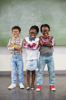 Portrait of three school kids standing with arms crossed against chalkboard in classroom