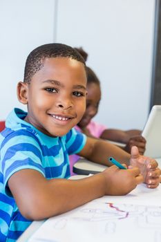 Portrait of smiling schoolboy doing homework in classroom at school