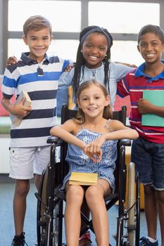 Portrait of smiling school kids standing with arm around in library at school