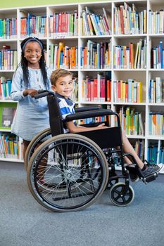 Portrait of schoolgirl standing with schoolboy on wheelchair in library