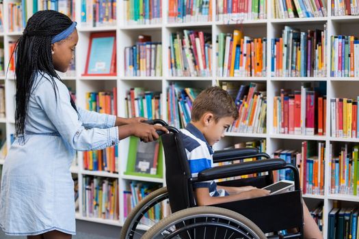 Schoolgirl pushing a boy on wheelchair in library
