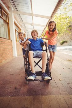 Happy school kids pushing a boy on wheelchair in school corridor