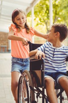 Happy schoolgirl pushing a boy on wheelchair in school corridor