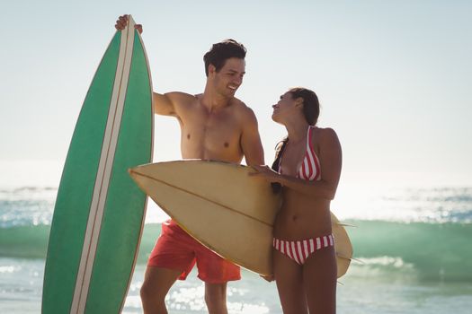 Romantic young couple standing with surfboard on beach