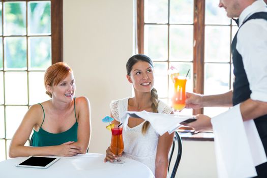 Waiter serving cocktail to two smiling women in restaurant