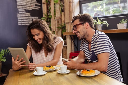 Young couple sitting at table using digital tablet in cafeteria