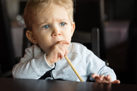 Baby boy sitting in high chair and plays with chopsticks at chinese restaurant.portrait horizontal.