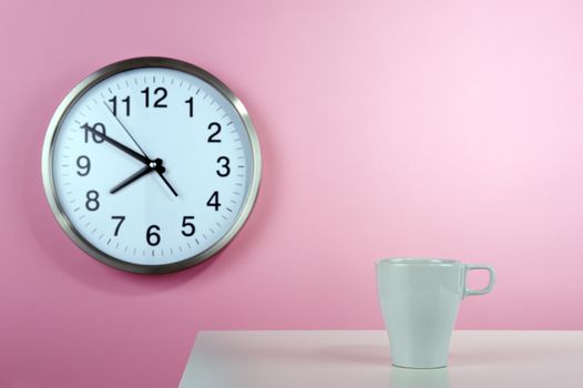 Empty white cup on the background of a pink wall with a clock