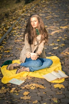 girl with a cup of coffee sitting in autumn Park