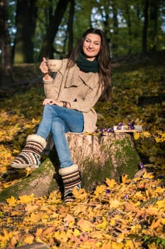 girl with a cup of coffee sitting on a tree stump in autumn Park