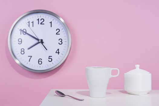 White cup of coffe on the background of a pink wall with a clock
