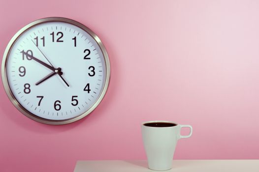 White cup of coffe on the background of a pink wall with a clock