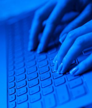 Woman fingers on the laptop keyboard in blue tones.