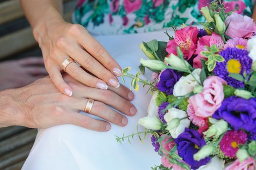 hands of bride and groom with rings and wedding bouquet.