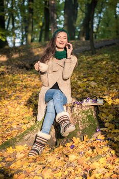 girl with a cup of coffee sitting on a tree stump in autumn Park