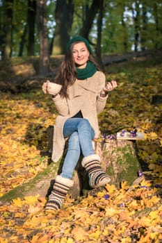 girl with a cup of coffee sitting on a tree stump in autumn Park