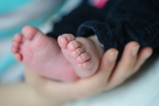 mother hands holding baby feet on bed