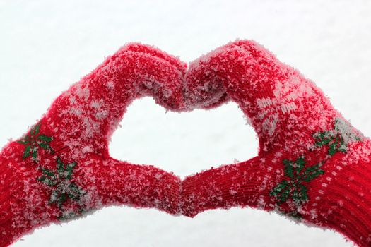 hands in snow-covered gloves in the form of heart against the background of snow