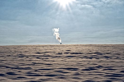 The smoking chimney in the distance in a snowy landscape
