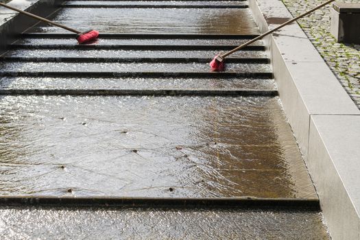 Two road brooms stand in a water channel.