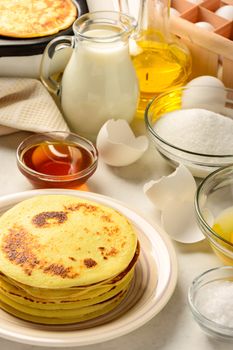 Pancakes and ingredients for making pancakes on a white background
