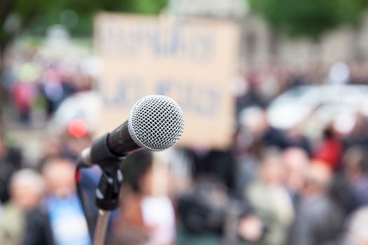 Microphone in focus, blurred crowd in background. Political rally.